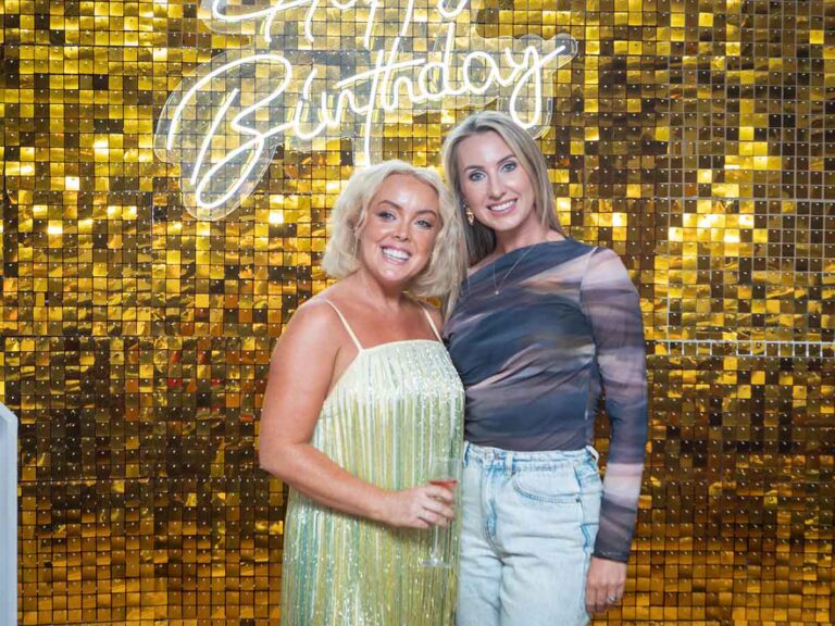Two friends smiling under a neon Happy Birthday sign at a private party in Dublin
